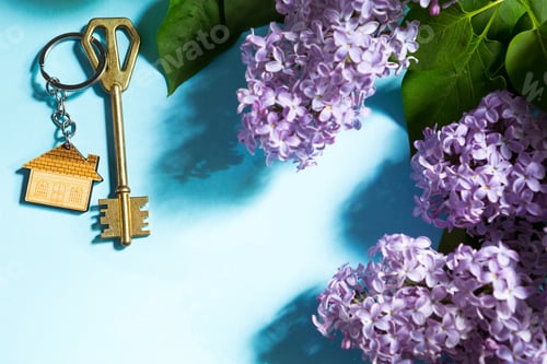 Preview: House key with keychain on blue spring background and lilac branches.