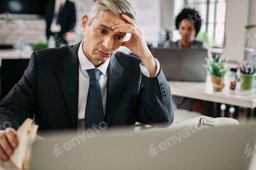 Preview: Worried businessman eating sandwich while using laptop in the office.