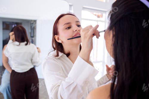 Preview: Young woman applying makeup to another woman in a bright