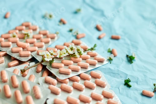 Preview: Pink Pills Arranged Neatly With White Blossoms on a Textured Blue Background