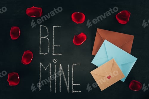 Preview: lettering BE MINE surrounded with rose petals and envelopes on black surface, st valentines day