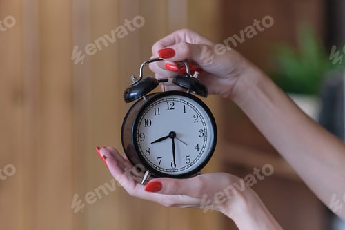 Preview: black alarm clock in woman hands, concept of menopause, or wasting time