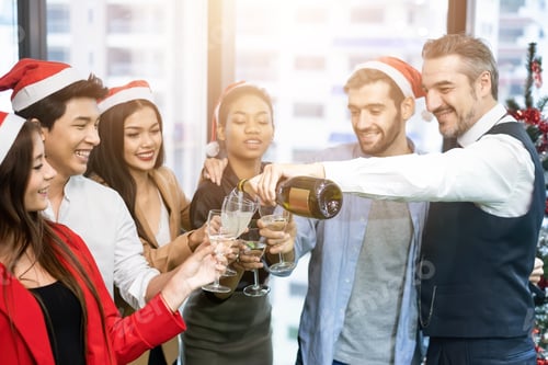 Visualização: Grupo de colegas se sentindo feliz com um sorriso servindo champanhe na festa de Natal no escritório.
