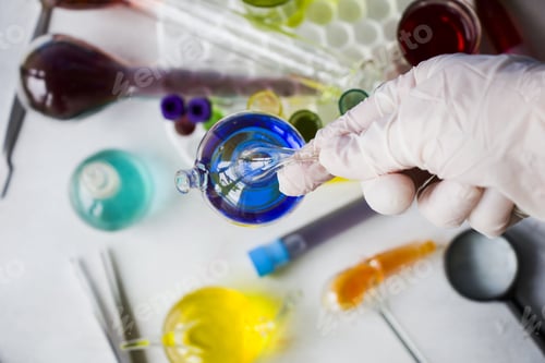 Preview: Selective top view of a hand in gloves holding laboratory glassware on blurred backgroun