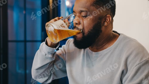 Preview: Middle-aged African American male drinking beer having fun happy night party event online at home.
