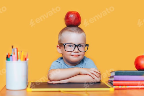 Preview: Happy cute clever boy is sitting at desk and smiling. Child is on a yellow background. First time to