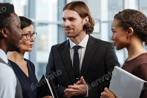 Preview: Smiling handsome businessman talking to group of colleagues at company office