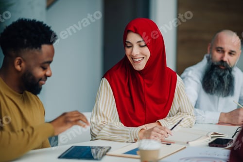 Preview: Smiling muslim businesswoman taking notes during a meeting with multi ethnic colleagues