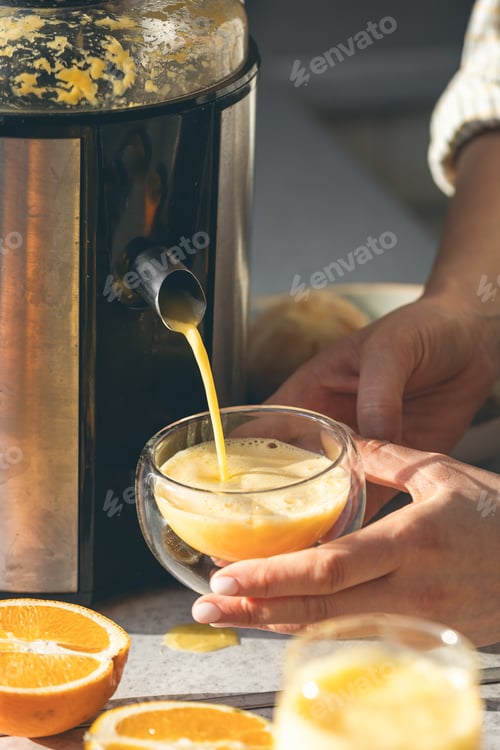 Preview: A woman preparing fresh orange juice for breakfast in kitchen.