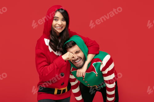 Preview: Cheerful couple dressed in Christmas funny sweaters having fun over red background.