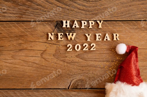 Visualização: Citação de letras de madeira de feliz ano novo de 2022 com chapéu de Papai Noel vermelho cintilante na mesa de madeira com glitter.