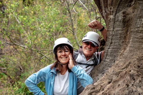 Preview: Smiling senior couple on mountain trekking day resting leaning against a tree trunk