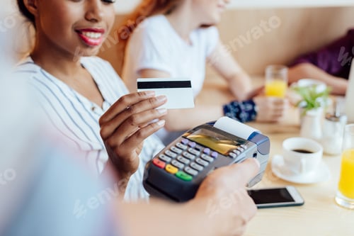 Preview: cropped shot of smiling african american girl holding credit card while waiter holding payment