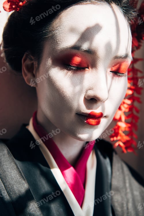 Preview: portrait of beautiful geisha with red and white makeup and closed eyes in sunlight with shadows