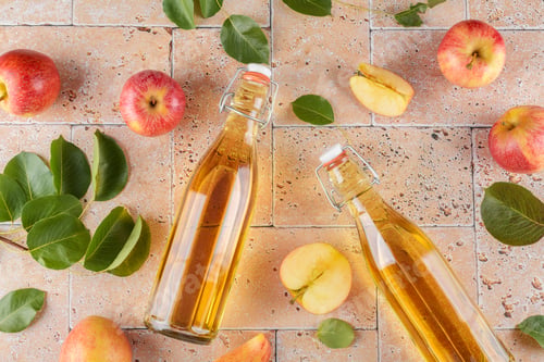 Preview: Apple cider vinegar in a two glass bottles and fresh apples with leaves on beige concrete background