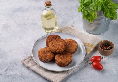 Preview: Chicken cutlets, fried, on a plate on a light background with fresh herbs, oil and tomatoes.