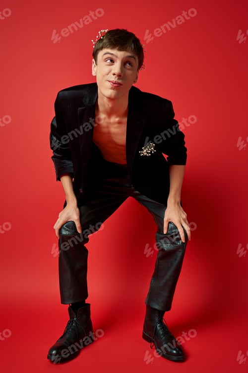 Preview: joyful man in stylish outfit with flowers in hair and pocket of velvet blazer looking away on red