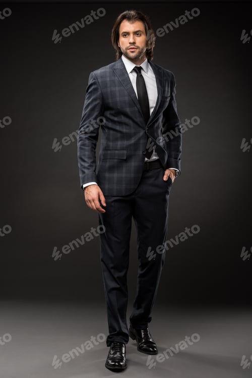 Preview: full length view of professional businessman in stylish suit standing with hand in pocket on black