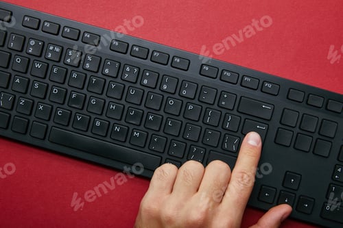 Preview: Top view of man pushing button on black computer keyboard on red background