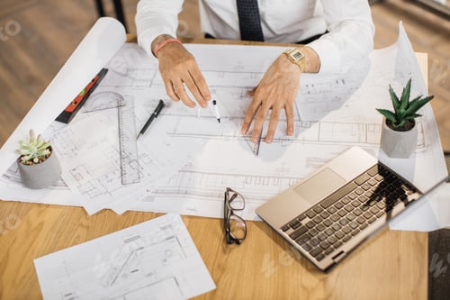 Preview: Close up of hands of architect, engineer or designer sitting at table and analysing blueprints