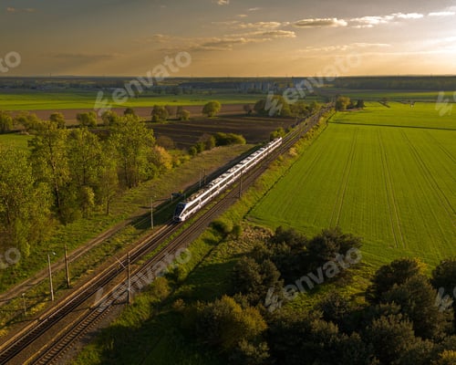 Preview: Aerial view of a train moving along railroad tracks surrounded by lush green fields