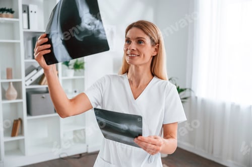 Preview: Checking x-ray. Young female doctor in white coat is indoors