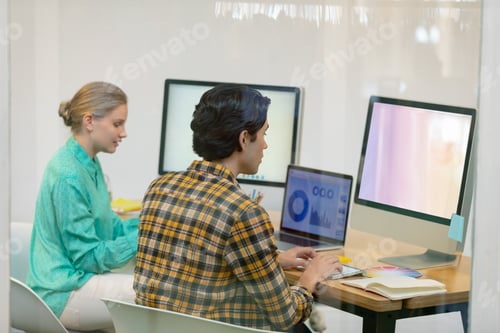 Preview: Rear view of Caucasian male and female graphic designer working on computer at desk in office