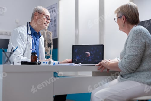 Preview: Medic showing coronavirus bacteria illustration on laptop to patient in cabinet
