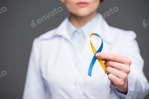 Preview: Female doctor holding blue and yellow ribbon for Down Syndrome Day isolated on grey
