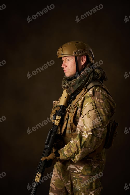 Preview: side view of a young military soldier with automatic airsoft rifle with telescopic sighting