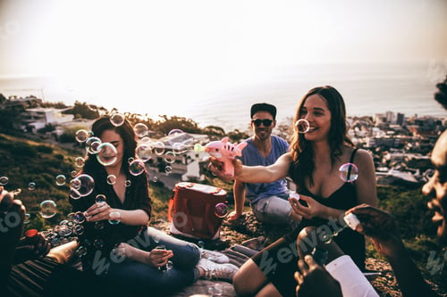 Preview: Group of young adult friends having fun blowing bubbles at picnic
