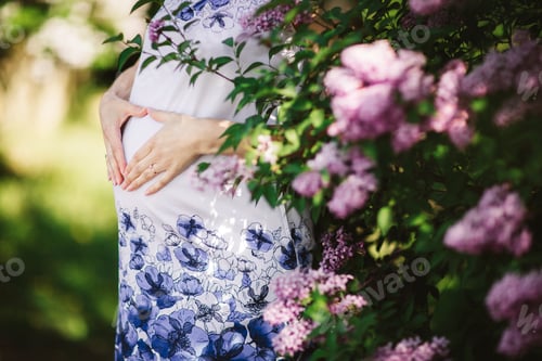 Preview: Young pregnant woman against blossoming tree in spring