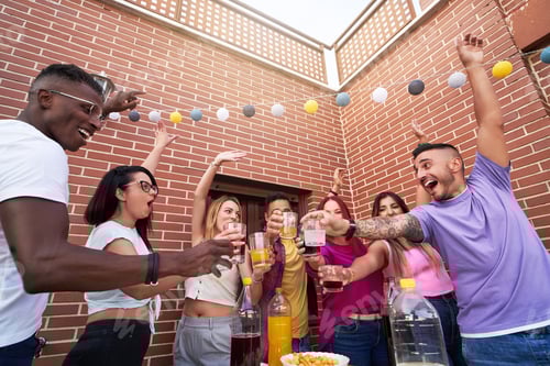 Visualização: Grupo de amigos felizes brindando com bebidas enquanto desfrutam de uma festa ao ar livre em um terraço.