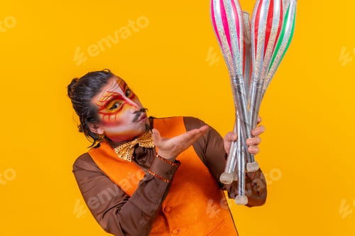 Preview: Cheerful circus performer skillfully holding a number of clubs isolated on yellow background