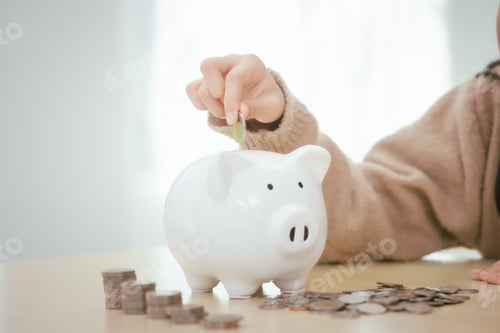 Preview: A girl sits at a table, saving money by inserting coins into piggy bank,emphasizing the importance