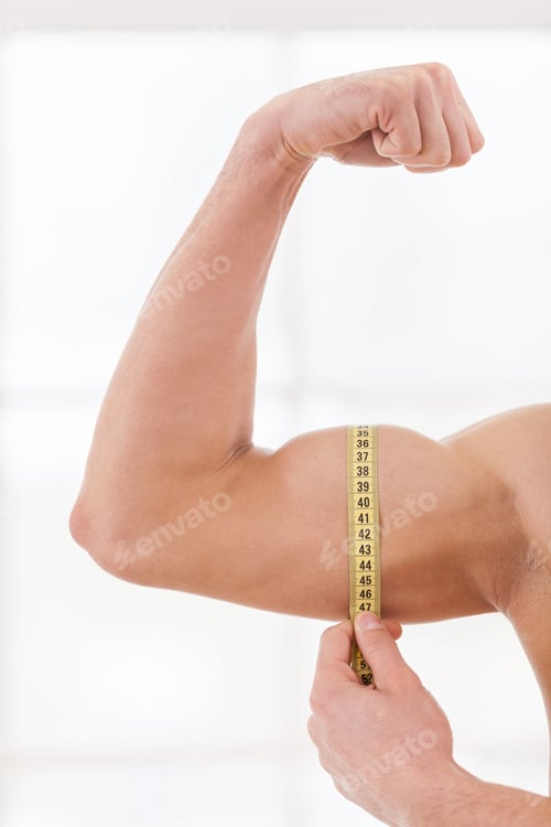 Preview: Perfect bicep. Cropped image of muscular man measuring his bicep with measuring tape