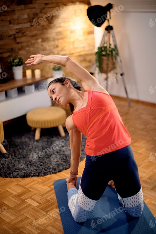 Preview: Mid adult sportswoman stretching during home workout.