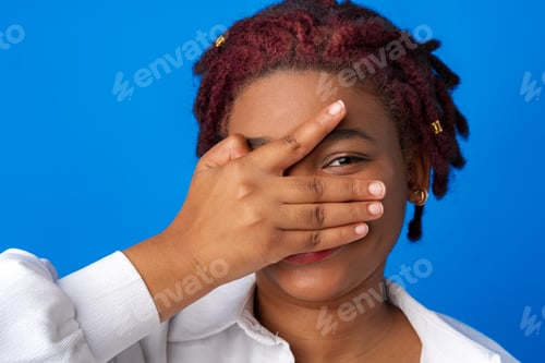 Preview: Funny afro woman peeping through the palm of her hand against blue background