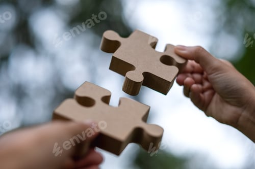 Preview: Closeup image of a couple people holding and putting a piece of wooden jigsaw puzzle together