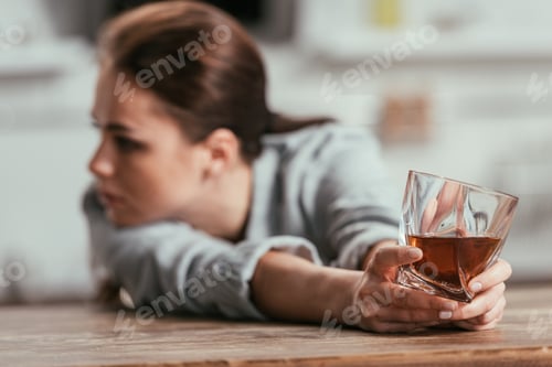Preview: Selective focus of sad woman holding whiskey glass at table