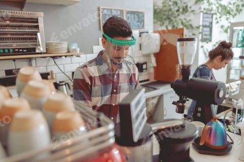 Preview: Smiling barista with mustache in protective visor preparing coffee