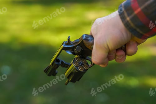 Preview: Unrecognizable man holding revolver with full cartridge in the drum Close-up.