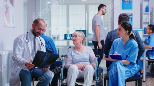 Preview: Doctor holding radiography of disabled senior woman in wheelchair