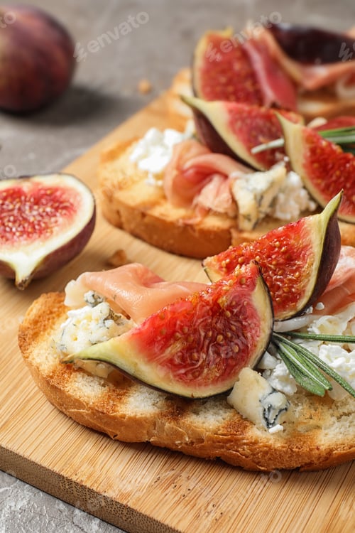 Preview: Bruschettas with cheese, prosciutto and figs served on wooden board, closeup