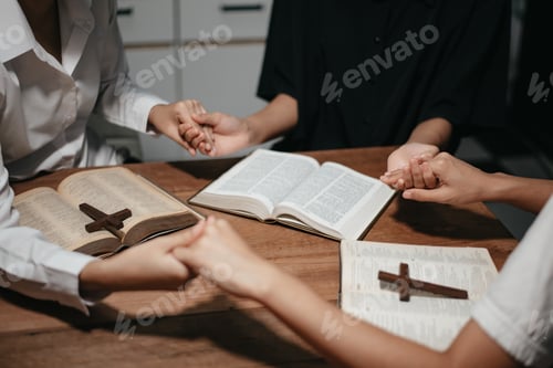 Preview: Group of Christians sit together and pray around a wooden table with blurred open Bible pages