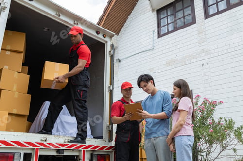 Preview: Young couple checks with two movers unloading boxes and furniture from a pickup truck