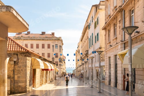 Preview: Sunlit cobblestone street lined with historic buildings and bustling with pedestrians