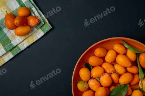 Preview: top view of fresh ripe kumquat fruits on a plate on black background with copy space