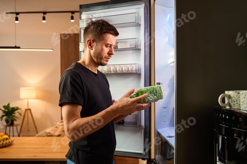 Preview: Man taking fresh greens from open refrigerator