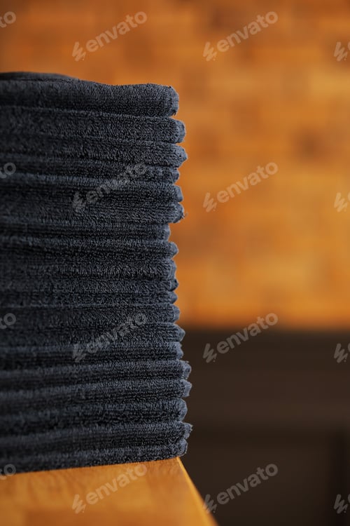 Preview: stacked black bathroom towels on a wooden table and brick wall background. spa salon, barbershop.